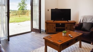 A living room with a TV on a wooden stand, a sofa, a coffee table with a plant, and a sliding glass door leading to a fenced outdoor area. - 3 bedroom accommodation in Caerarfon (Caerarfon)