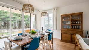 Zona pranzo con tavolo in legno apparecchiato per quattro persone, sedie blu e un mobile contenitore in legno con vetri.