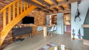 Una cocina moderna con vigas de madera, un comedor con mesa y sillas de madera, y una escalera con barandillas de madera.