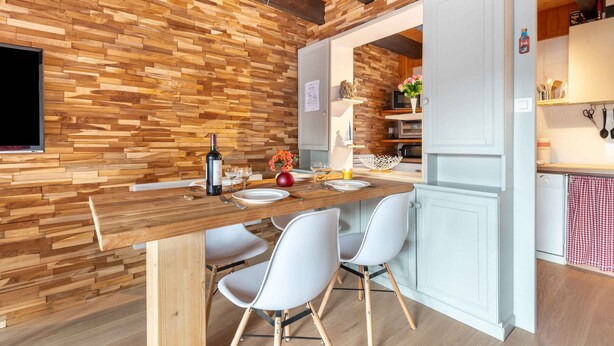 Una cocina moderna con una pared de madera, armarios blancos y un área de comedor con una mesa de madera y sillas blancas.