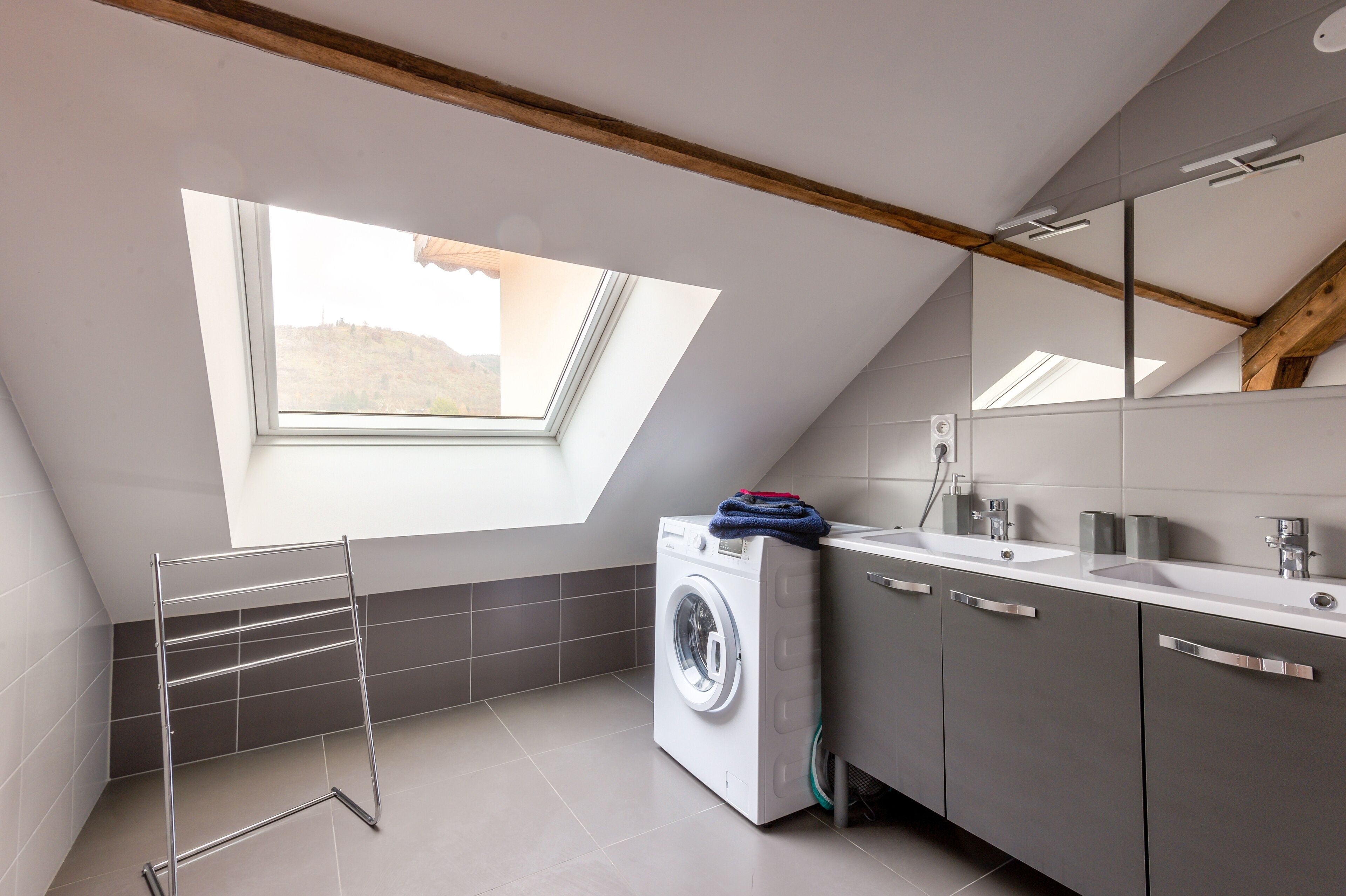 A modern bathroom with a skylight, a washing machine, and a large mirror.