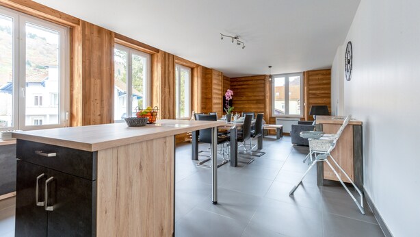 A modern kitchen with wooden accents, a central island, and a dining area with chairs and a table. - Ouréa - duplex avec balcon (La Bresse)