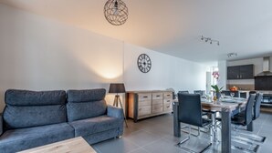 A modern living room with a grey sofa, a wooden coffee table, and a dining area with a wooden table and chairs. - Ouréa - duplex avec balcon (La Bresse)