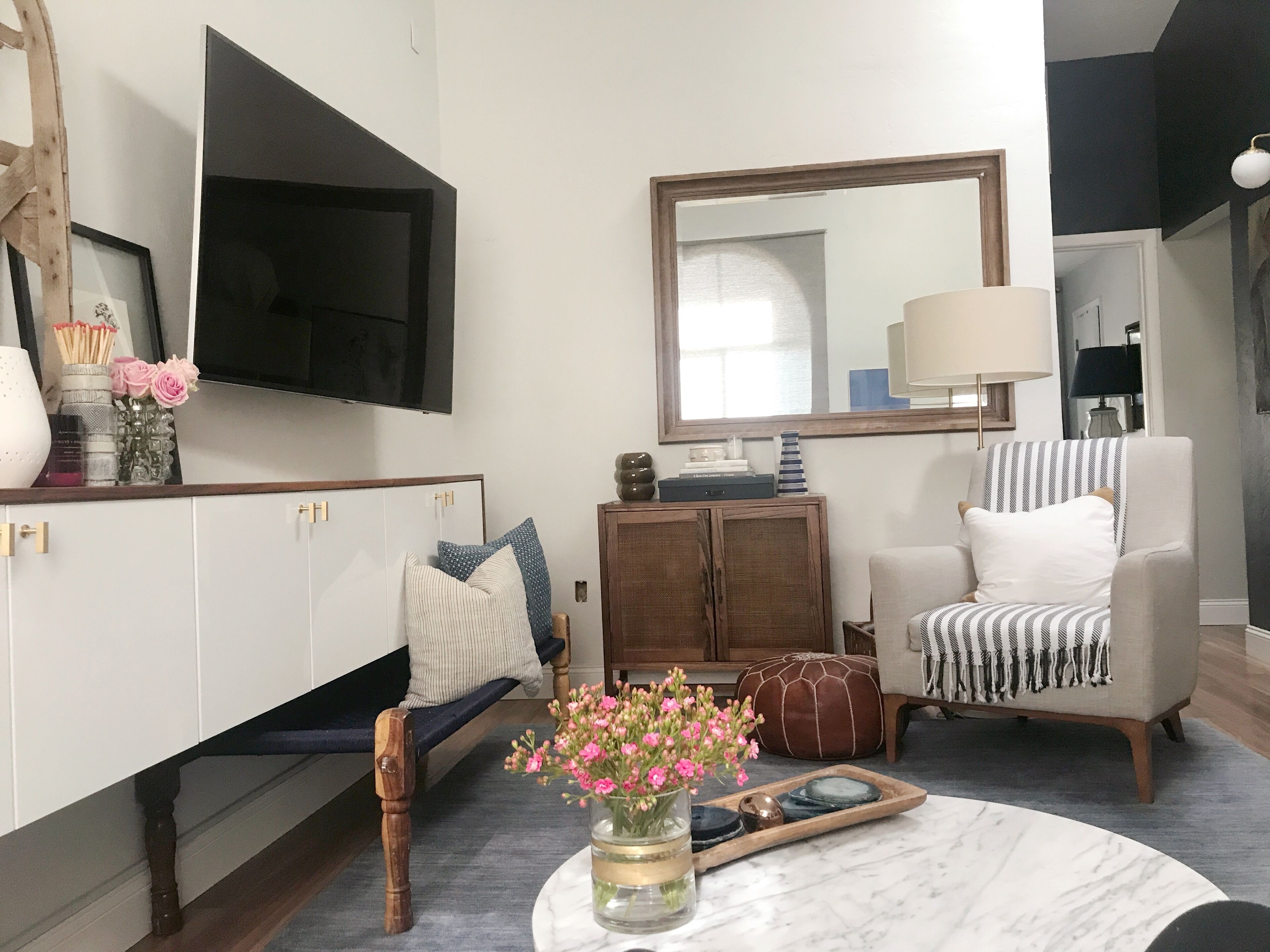 A living room with a sofa, armchair, TV, and a coffee table with flowers.