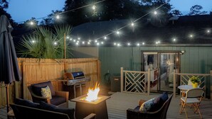 An outdoor deck with a fire pit, wicker furniture, and string lights. - Peaceful modern and close to everything (Gainesville)