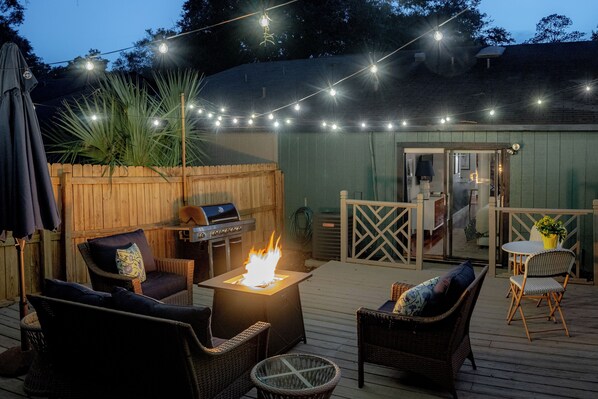 An outdoor deck with a fire pit, wicker furniture, and string lights. - Peaceful modern and close to everything (Gainesville)