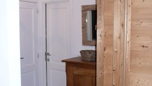 Un corridoio con due porte bianche, un mobile in legno con uno specchio e un pavimento piastrellato scuro.