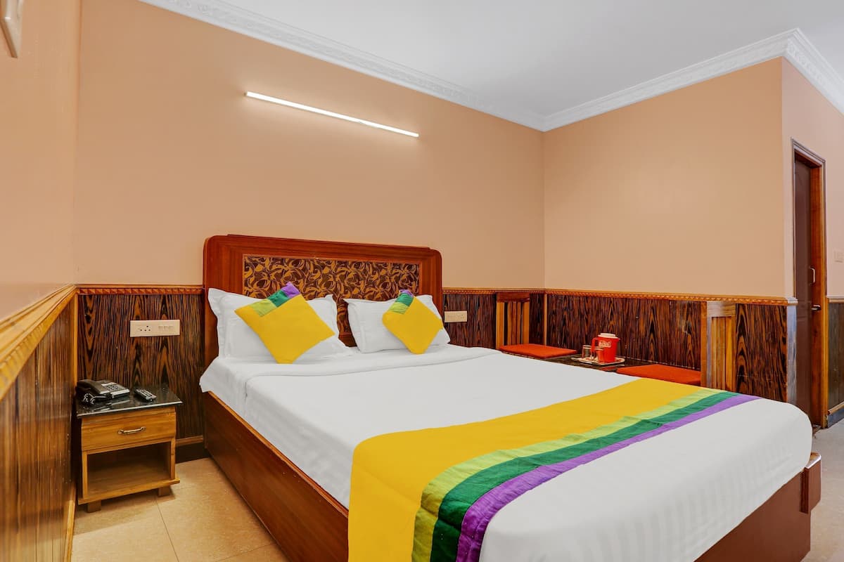 A hotel room with a wooden headboard, a bed with white bedding, a bedside table with a phone, and a nightstand.