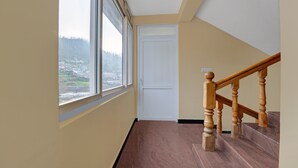 Un pasillo con una escalera de madera, una puerta blanca y un ventanal con vistas a un paisaje montañoso.