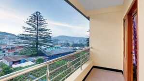 Un balcón con barandilla de metal que da a un barrio residencial con casas y un árbol grande.