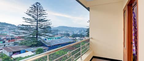 A balcony with a metal railing overlooking a residential area with houses and a large tree.