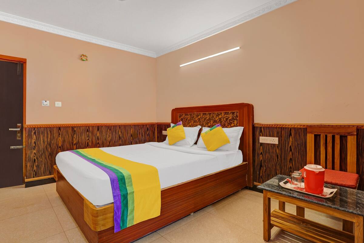 A neatly made bed with a rainbow blanket, wooden headboard, and a bedside table with a tray.