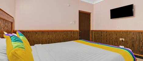 A hotel room with a large bed, a wooden headboard, a television mounted on the wall, and a door.