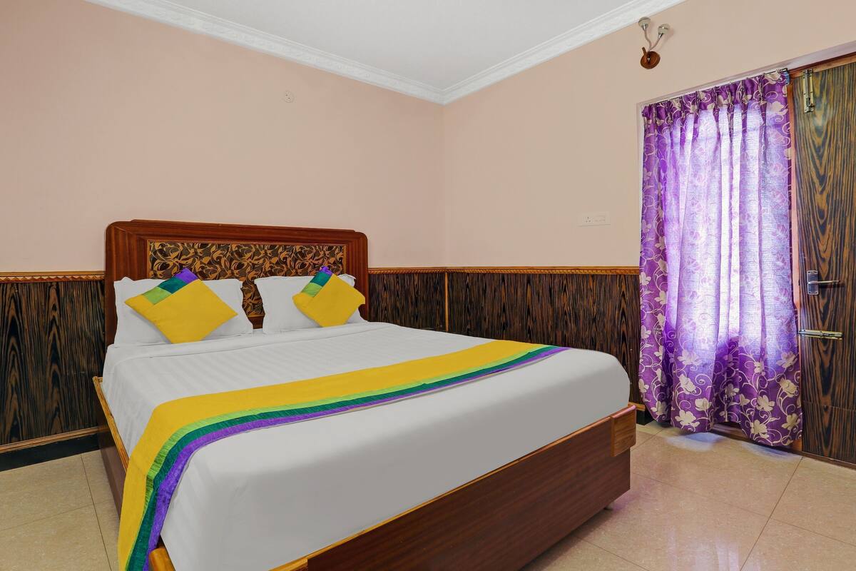 A neatly made bed with a wooden headboard, a purple curtain, and a wooden door.