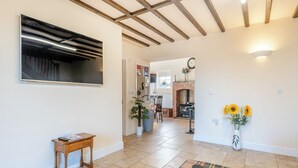 Ein geräumiger Wohnbereich mit Kamin, einem Esstisch mit Tee-Service und einem an der Wand befestigten Fernseher.