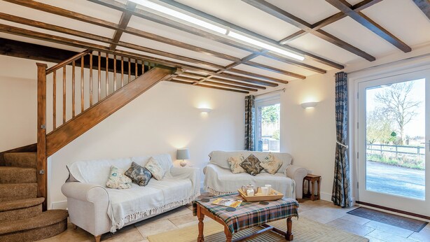 Ein Wohnzimmer mit Treppe, zwei Sofas, einem Couchtisch und Blick durch ein großes Fenster.