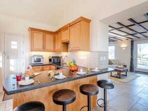 Eine moderne Küche mit Holzausbau, einer zentralen Kochinsel mit Barhocker, einer Mikrowelle und einem Essbereich mit einer Couch.