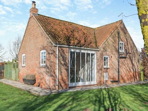 A brick house with a sloped roof, large glass doors, and a chimney. - One Chainbridge Barns (Skegness)