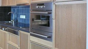 Eine moderne Küche mit Holzschränken, Edelstahlgeräten und einer blaumetallierten Spritzschutzwand.