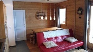 Ein gemütliches Blockhauss-Interieur mit einer roten Ledersofa, Holzwänden, einem Esstisch und Pendelleuchten.