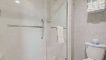 A modern bathroom with a glass shower enclosure, a white toilet, and a towel rack with folded towels.