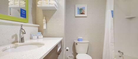 Une salle de bain avec un lavabo, des toilettes et une baignoire. On y trouve un porte-serviettes avec des serviettes pliées, un tableau accroché au mur et une poubelle.