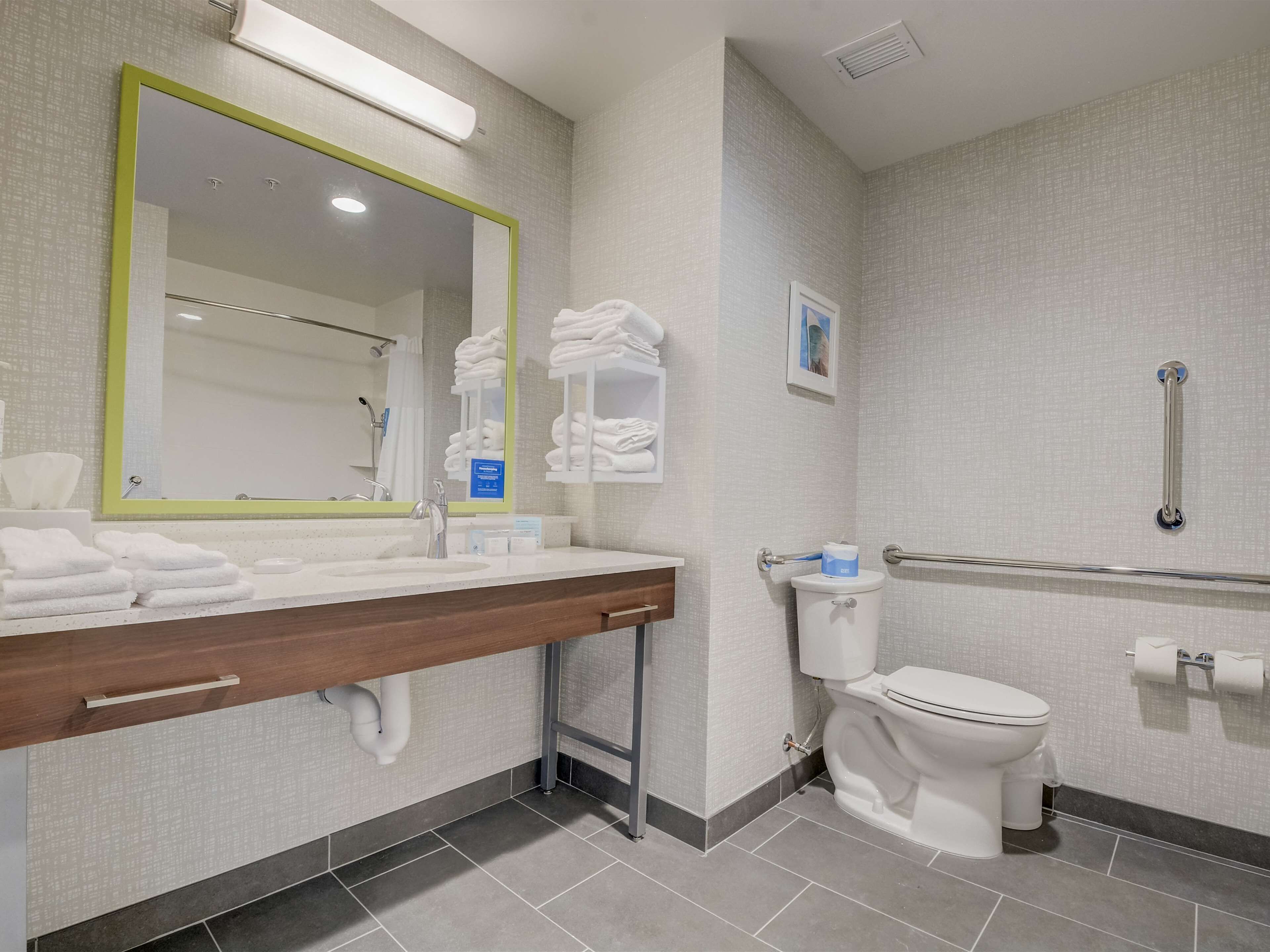 Un baño moderno con un espejo grande, un lavabo con toallero, un inodoro y una zona de ducha.