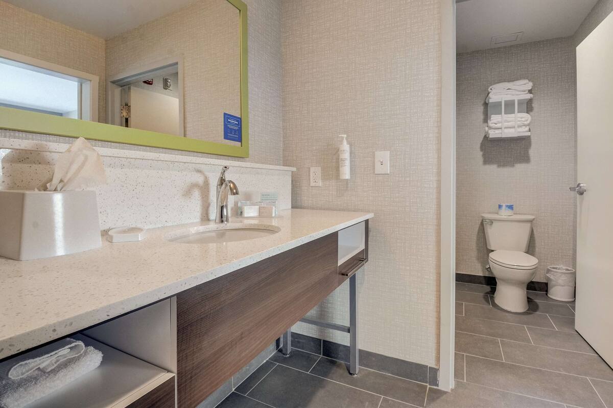 A modern bathroom with a large mirror, a sink, and a toilet.