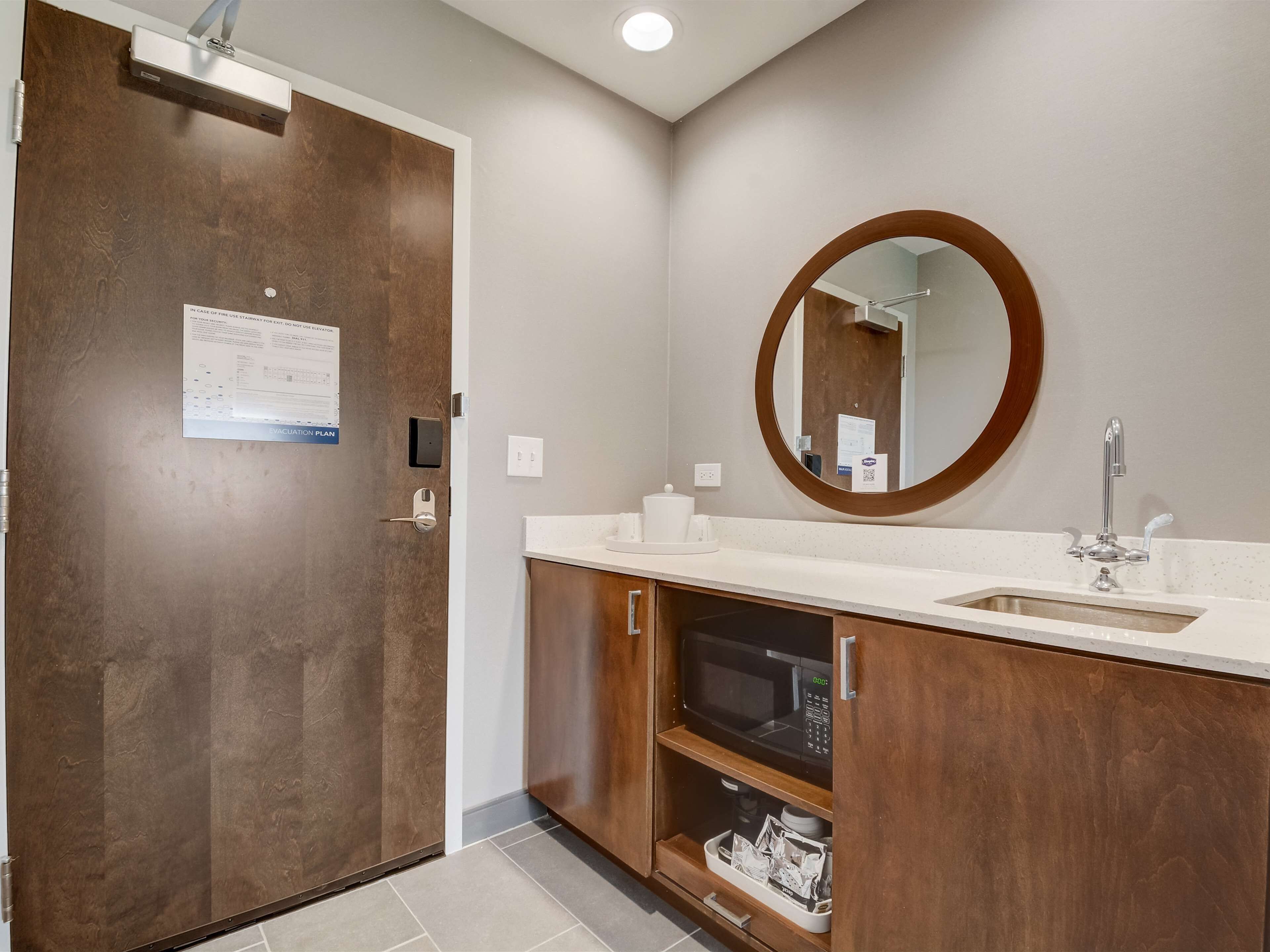 A modern bathroom with a wooden vanity, a built-in microwave, and a large mirror.