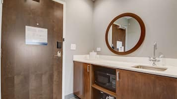 A modern bathroom with a wooden vanity, a built-in microwave, and a large mirror.