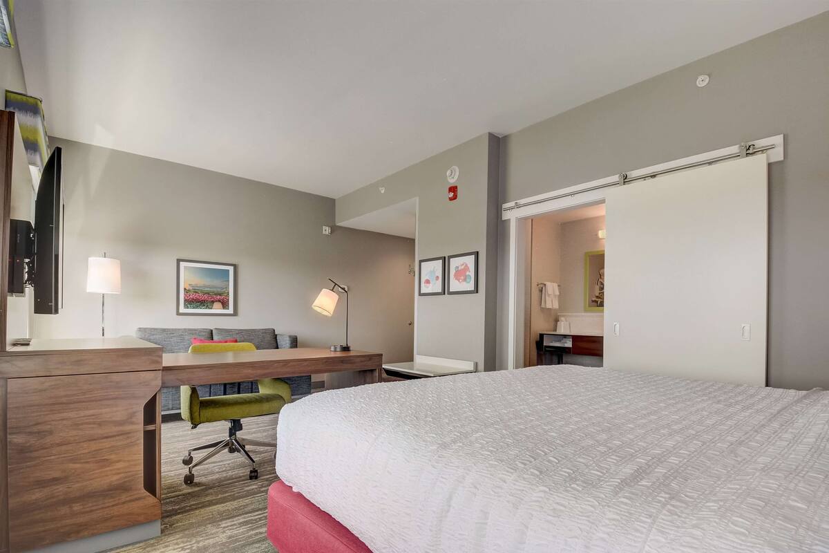 A hotel room with a large bed, a desk with a chair, a flat-screen TV, a lamp, and a painting on the wall.