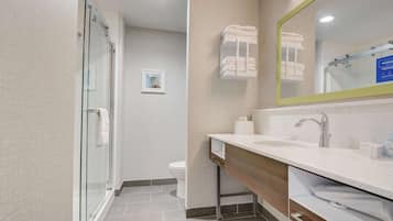 Un baño moderno con cabina de ducha de vidrio, tocador de madera con lavamanos y espejo, y un inodoro.