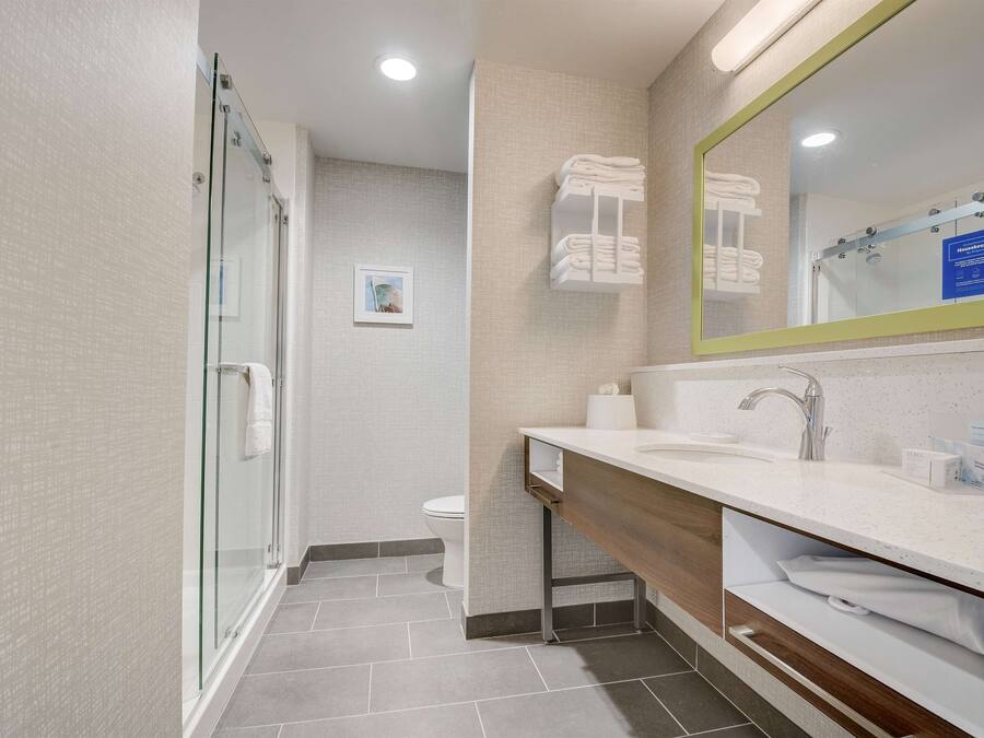 Un baño moderno con cabina de ducha de vidrio, tocador de madera con lavamanos y espejo, y un inodoro.
