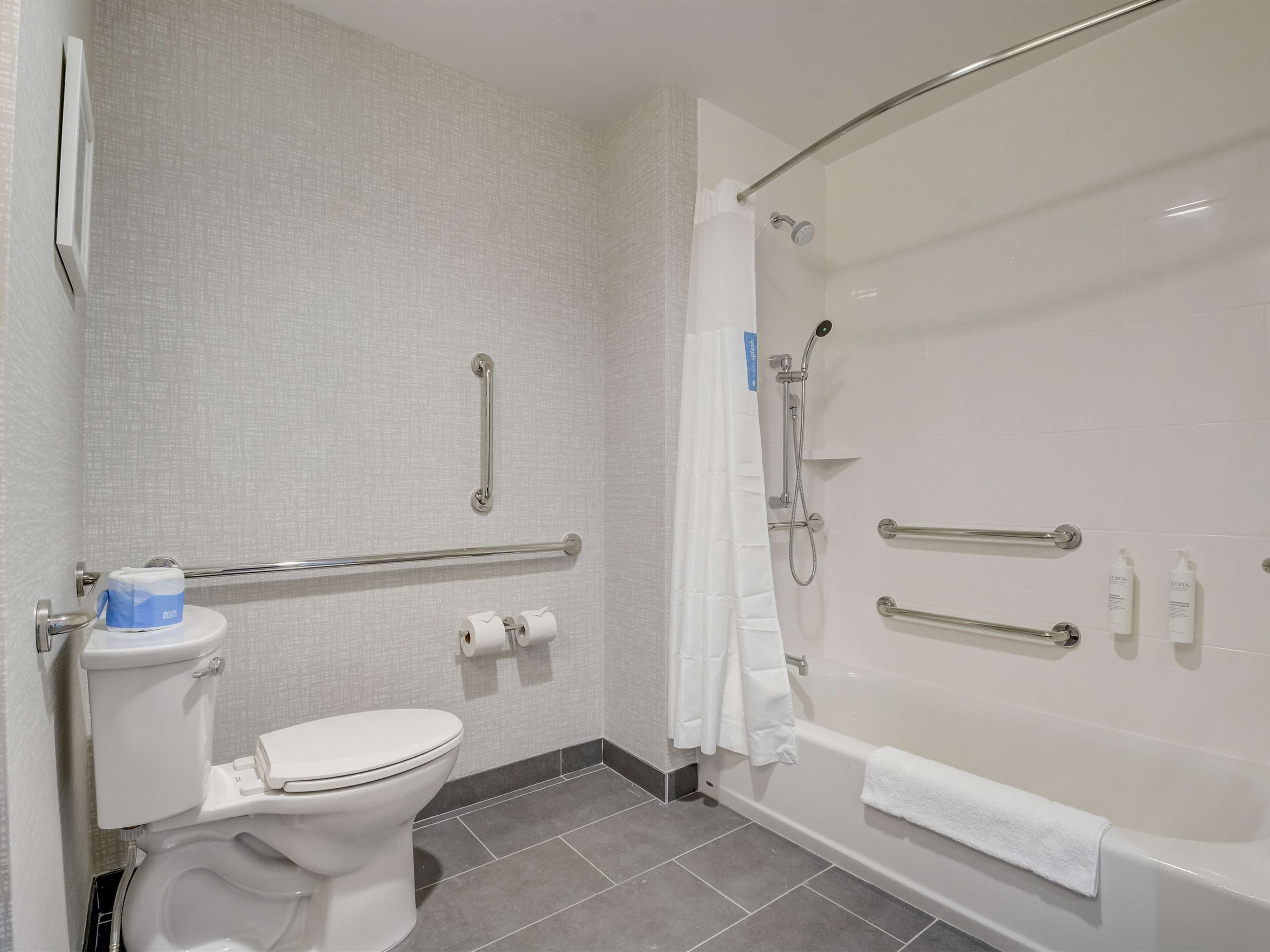A bathroom with a toilet, a bathtub with a shower, and grab bars.
