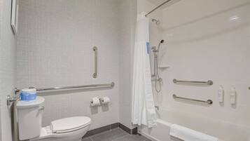 A bathroom with a toilet, a bathtub with a shower, and grab bars.