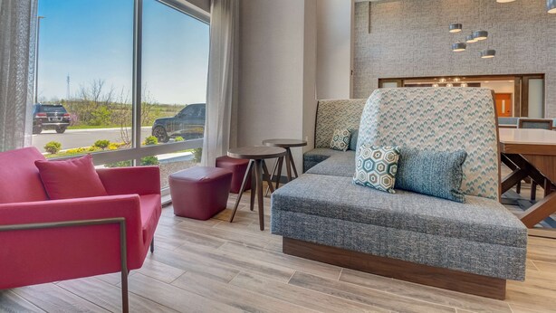 A modern hotel room with a large window, a red sofa, a grey armchair, and a small table.