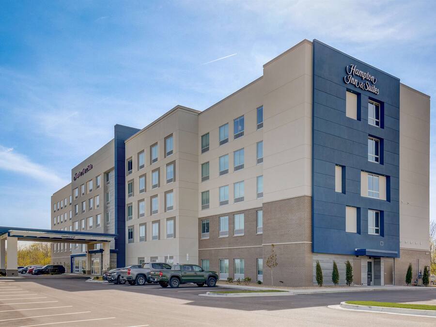Un hotel Hampton Inn & Suites con un diseño moderno, que cuenta con un amplio estacionamiento y varios accesos.