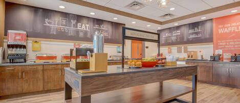 A modern breakfast area with a coffee machine, a fruit bowl, and a waffle station.
