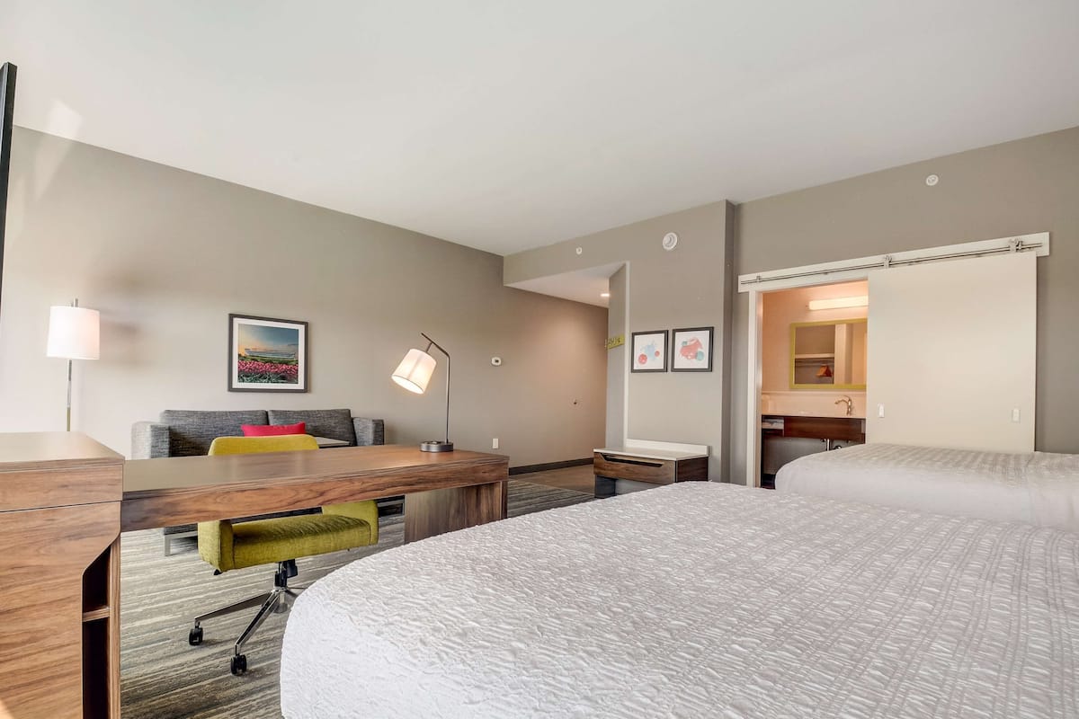 A hotel room with a large bed, a desk with a lamp, a sofa, and a small table.