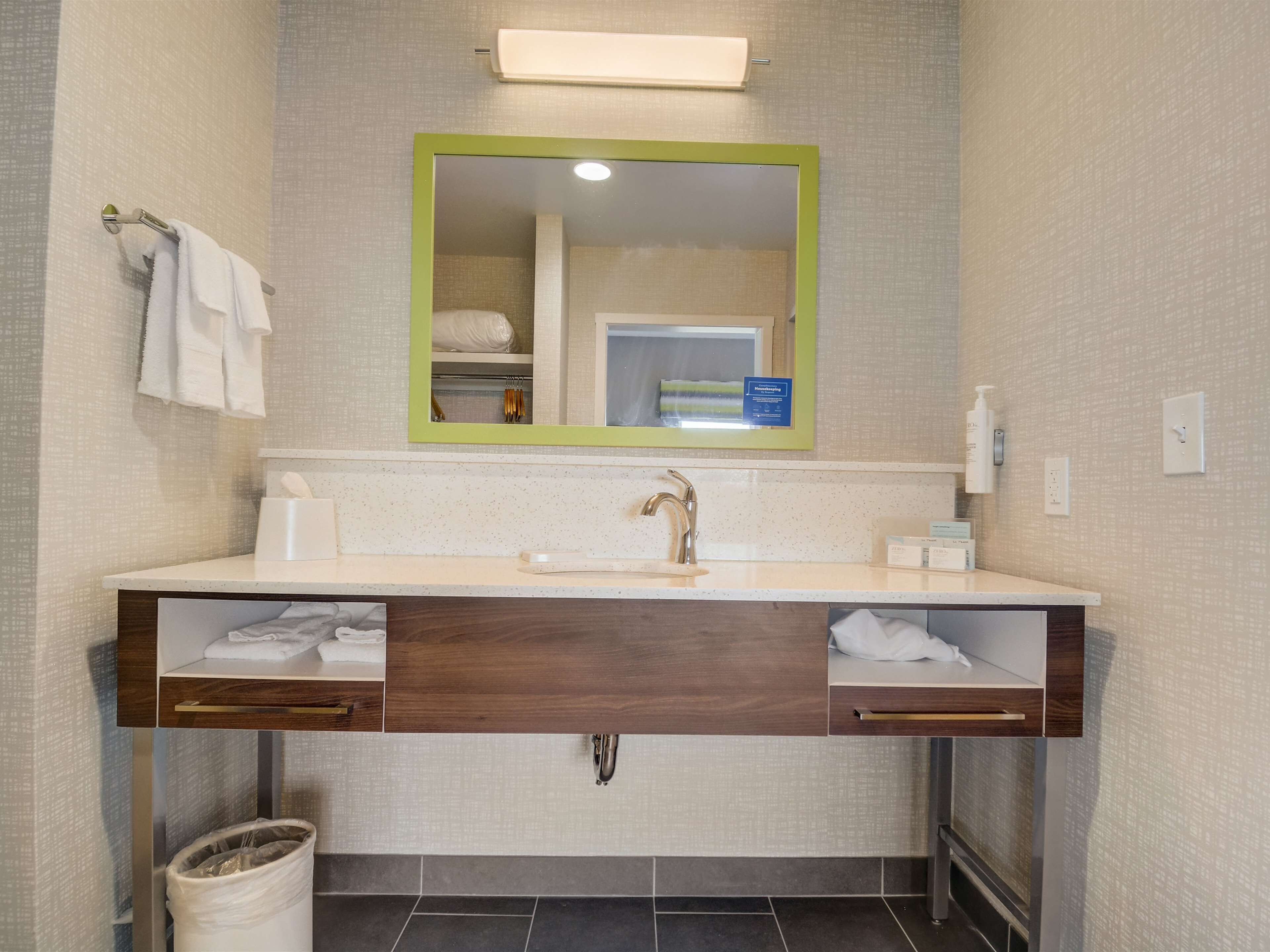 A modern bathroom with a wooden vanity, a mirror with a green frame, and a towel rack.