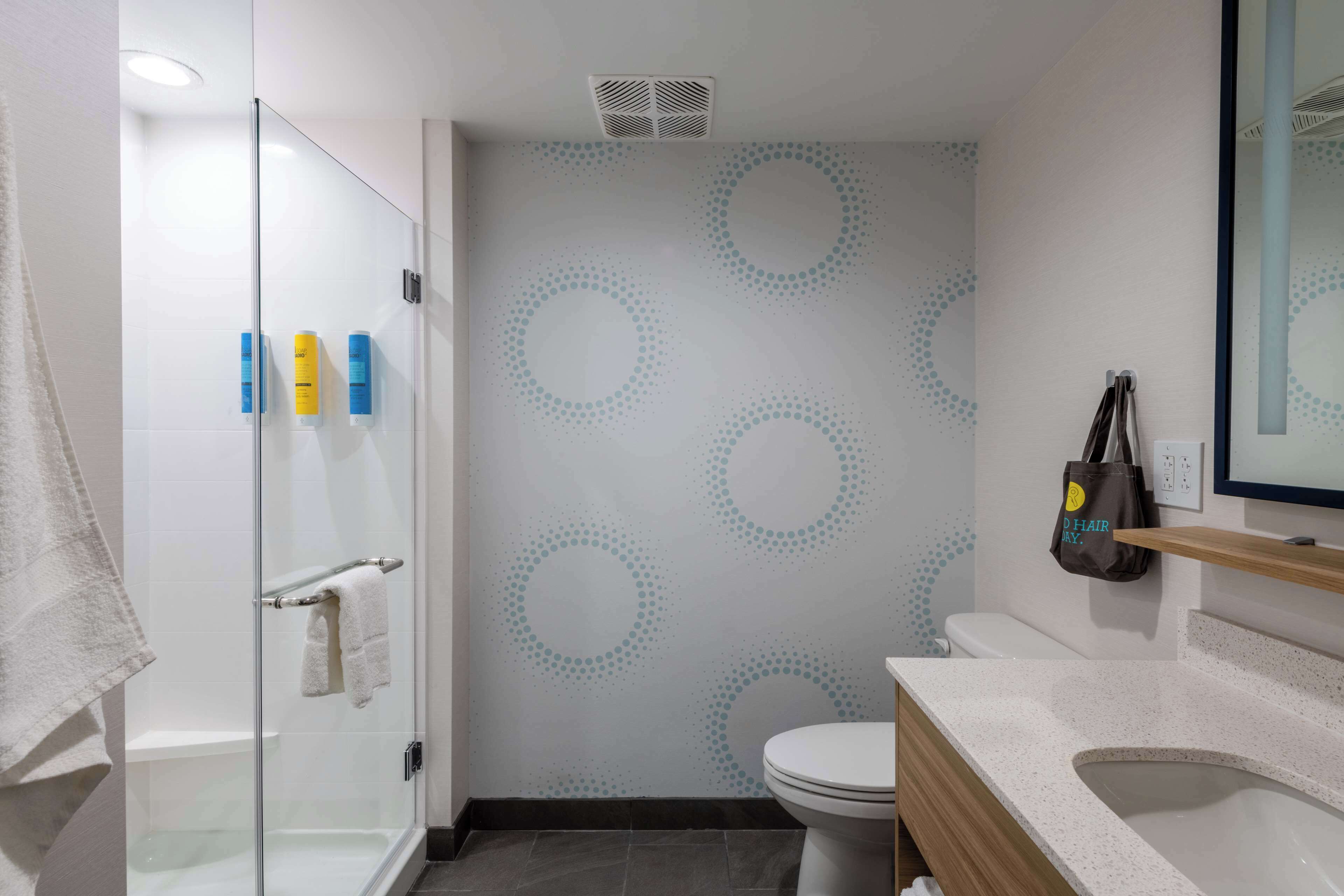 Un baño moderno con cabina de ducha de vidrio, inodoro y lavamanos con encimera de aspecto moteado.