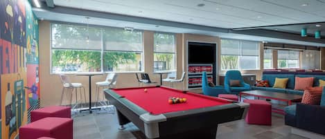 A pool table with red felt, surrounded by red and blue seating, and a colorful mural on the wall.