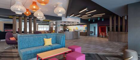 A modern lobby with a blue sofa, pink ottomans, and unique pendant lights.