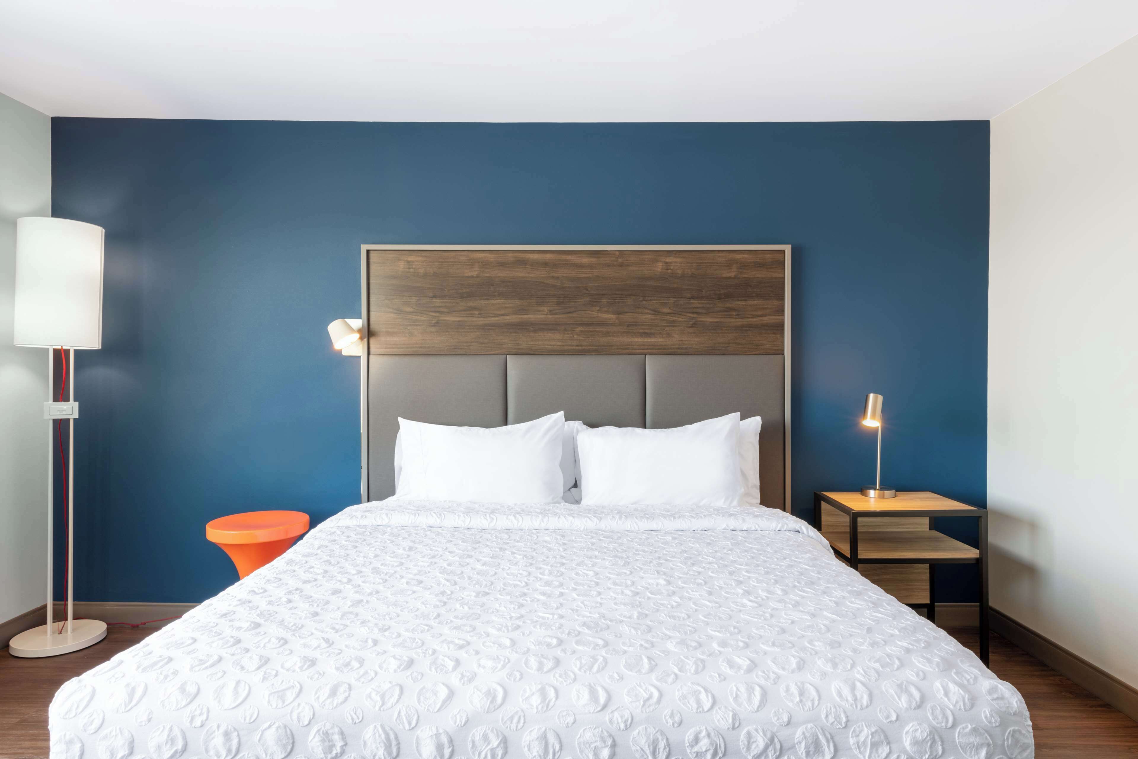 A hotel room with a large bed, a wooden headboard, a nightstand with a lamp, and a floor lamp.