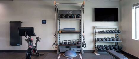 A gym with exercise equipment, a TV, and dumbbells on shelves.