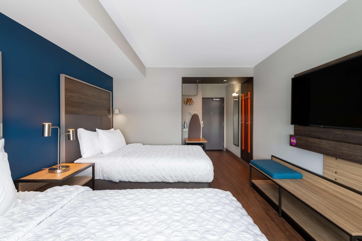 A hotel room with two beds, a TV, a desk, and a bench.