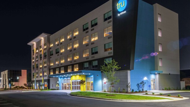 A modern hotel with a prominent 'tru by Hilton' sign, multiple floors, and a well-lit entrance. - Tru By Hilton Fayetteville Fort Bragg (Fayetteville)