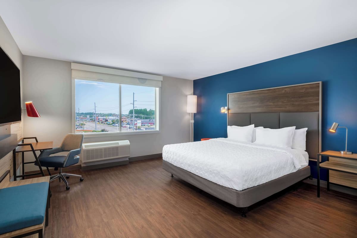 Quarto de hotel com uma cama grande, uma escrivaninha, uma cadeira, uma janela com vista para a cidade e uma televisão fixada na parede.