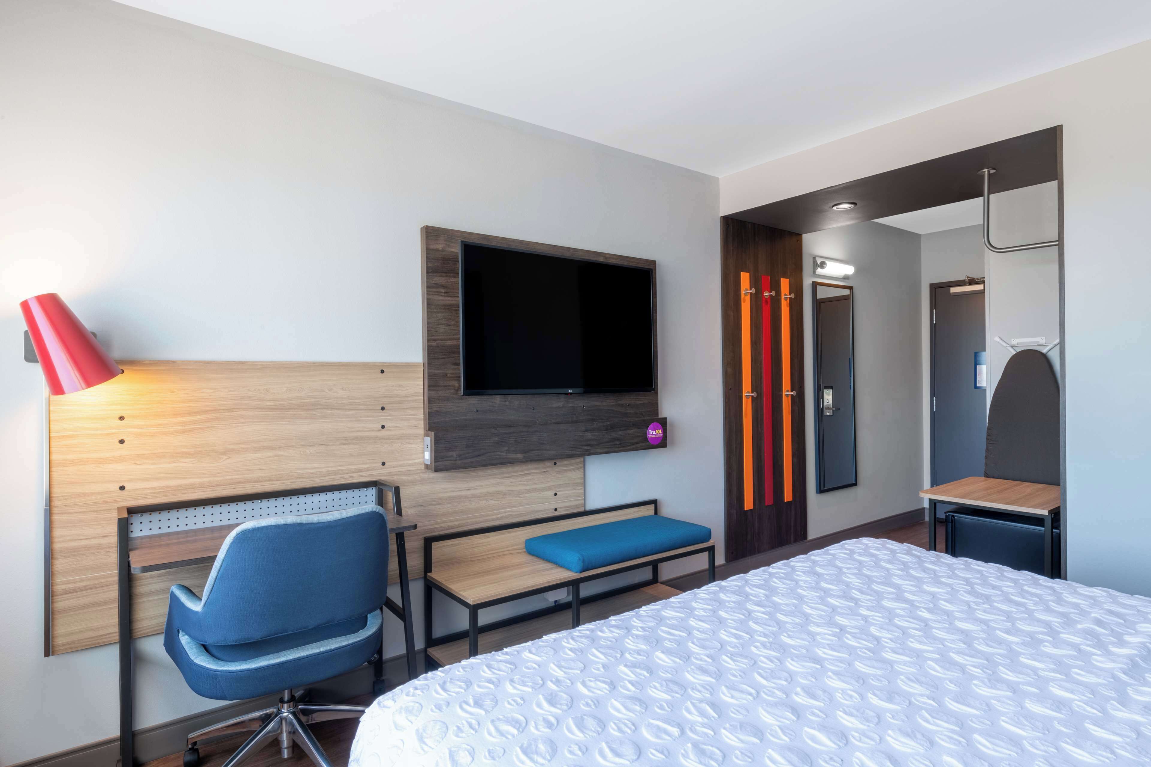Una habitación de hotel con cama, escritorio con silla, televisor montado en la pared y espejo.