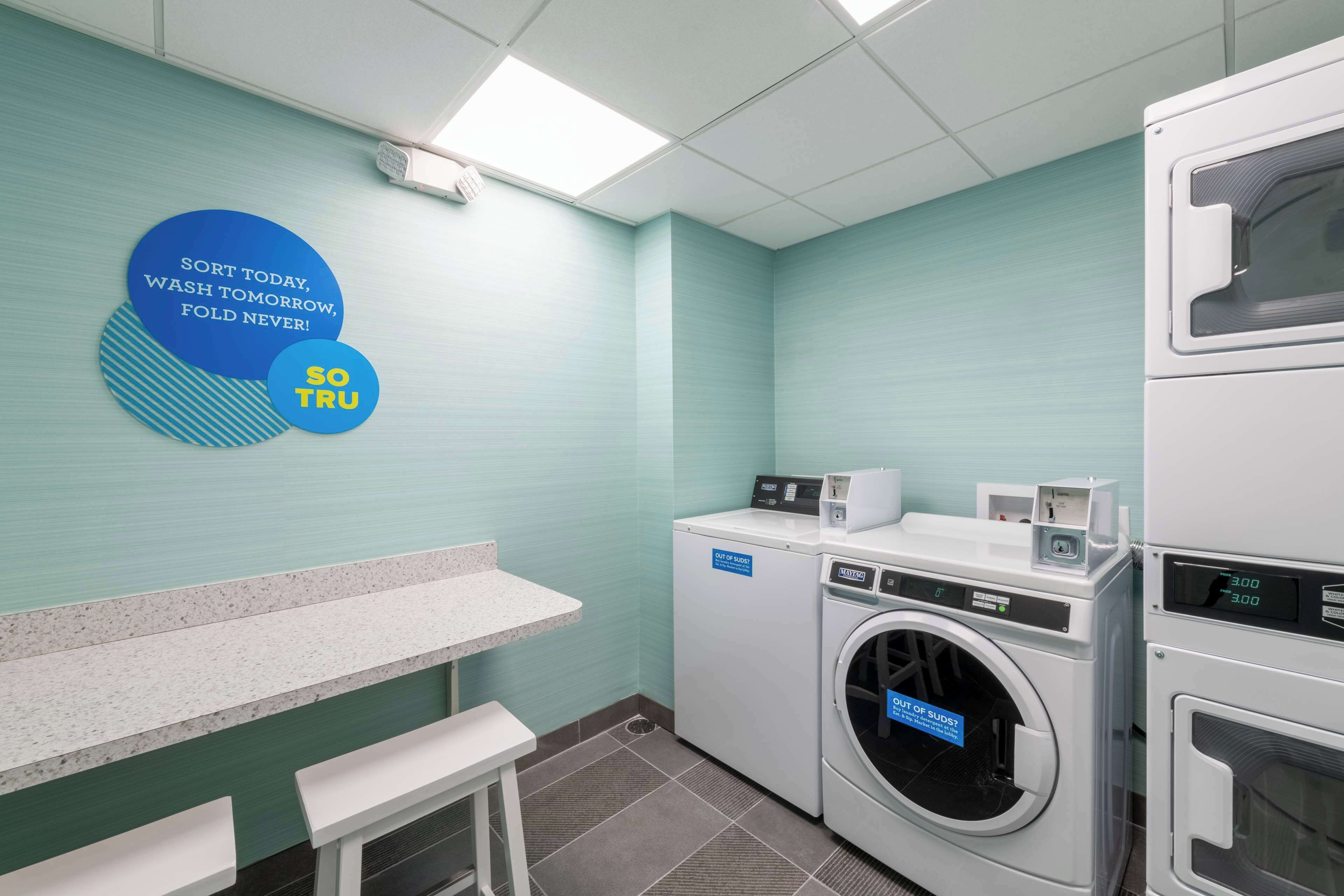 Une buanderie équipée d’un lave-linge, d’un sèche-linge et d’un banc. Un panneau affiché au mur porte un message motivant.